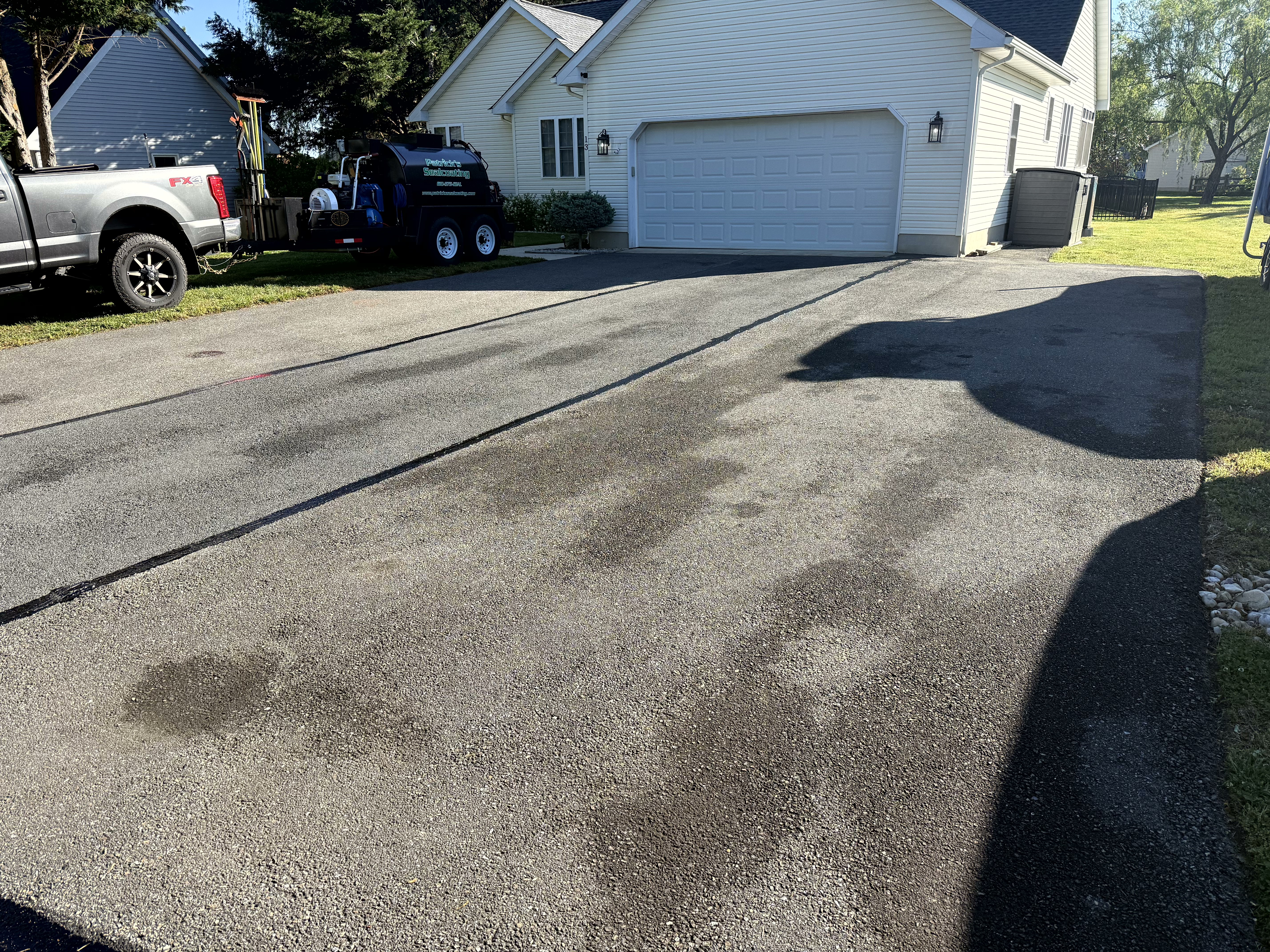 Freshly sealed two-car driveway with Patrick's Sealcoating trailer on site
